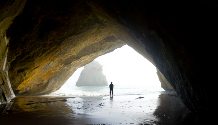 Colour photo from Te Whanganui-a-Hei (Cathedral Cove) Marine Reserve on the Coromandel Peninsula. It shows a person standing at the entrance of a large cave — looking towards Te Hoho Rock.