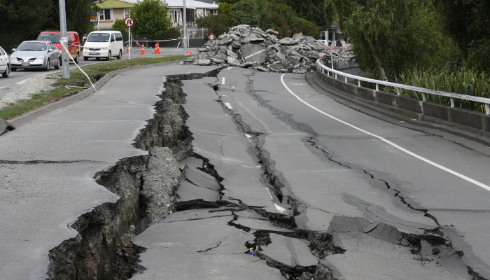 Colour photo of Fitzgerald Avenue in Christchurch after an earthquake. There are large cracks on the road and rubble in the background.
