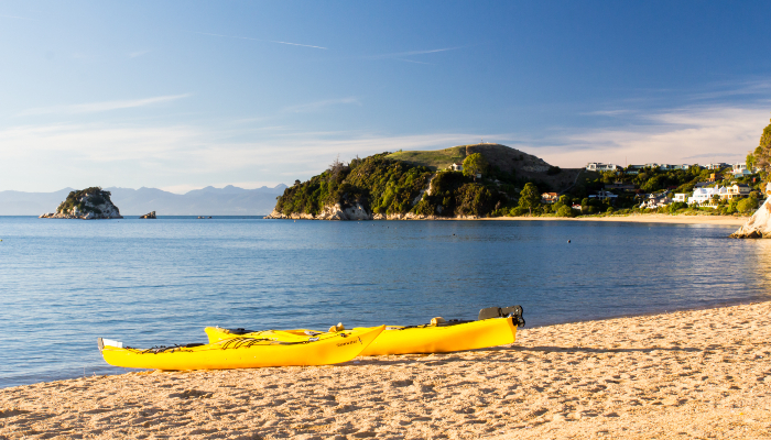 Colour photo of a clear sunny day at Kaiteriteri beach. Two yellow kayaks sit side by side on the shore.