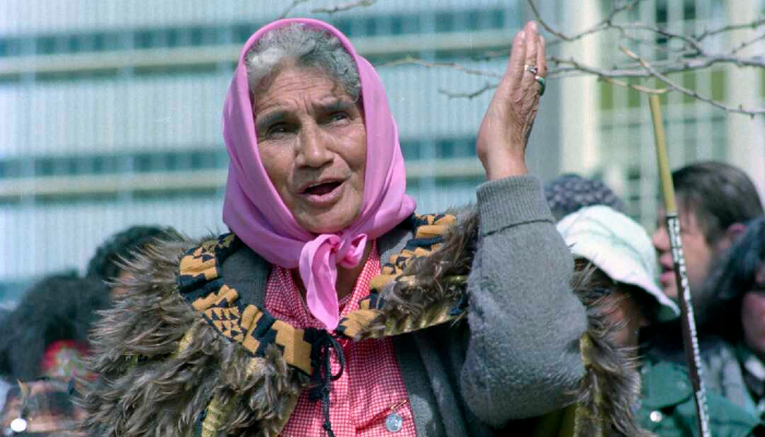 Colour photo of Dame Whina Cooper during the Māori Land March, in Hamilton, Aotearoa NZ. She is wearing a pink headscarf and a kahu kiwi (kiwi feather cloak).