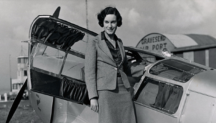 Black and white photo of Jean Batten standing with her Percival Gull aircraft.