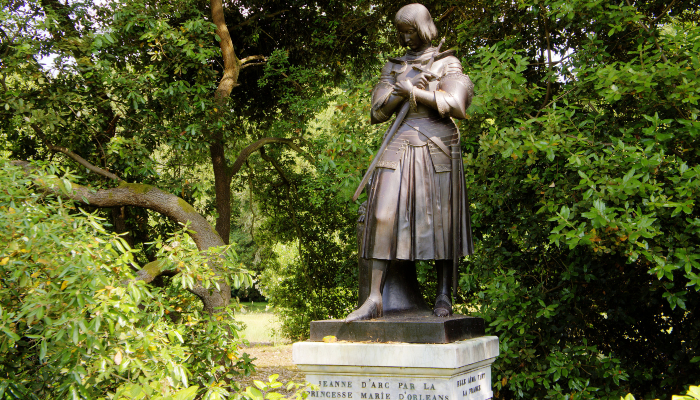 Colour photo of a bronze statue of Joan of Arc on a marble pedestal with her name.