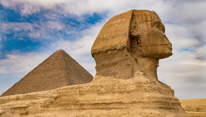 Colour photo of an ancient statue in Egypt called the Sphinx of Giza, with a pyramid in the background.