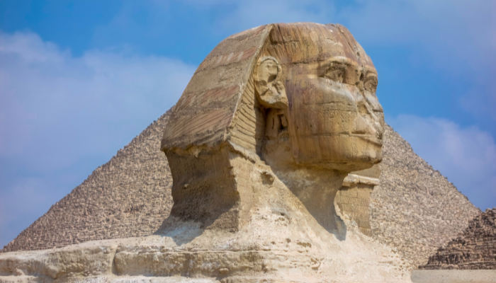 Colour photo of an ancient statue in Egypt called the Sphinx of Giza, with a pyramid in the background.