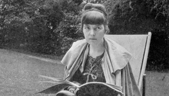 Black and white photo from 1916 or Katherine Mansfield. She is seated, book in hand, in a deck chair, Garsington Manor, England.