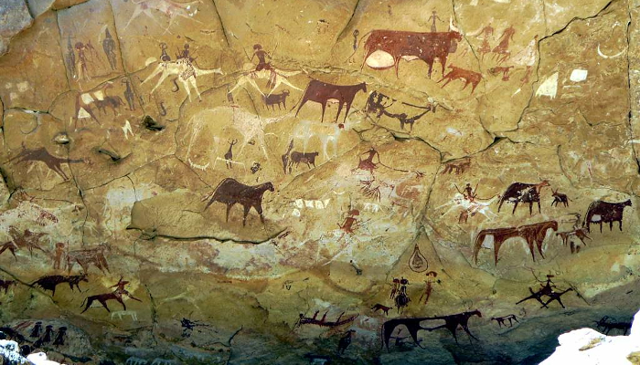 Colour photo of cave art on a rock face in Chad, Central Africa, showing brown and white coloured shapes of people and animals.