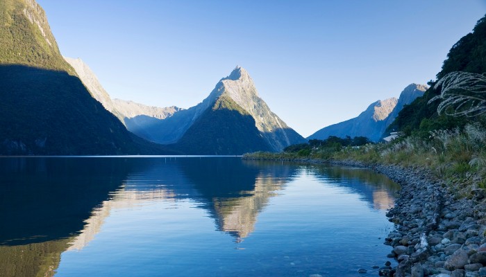 Colour photo taken from the edge of Milford Sound, Aotearoa NZ, showing Mitre Peak reflected in the water.