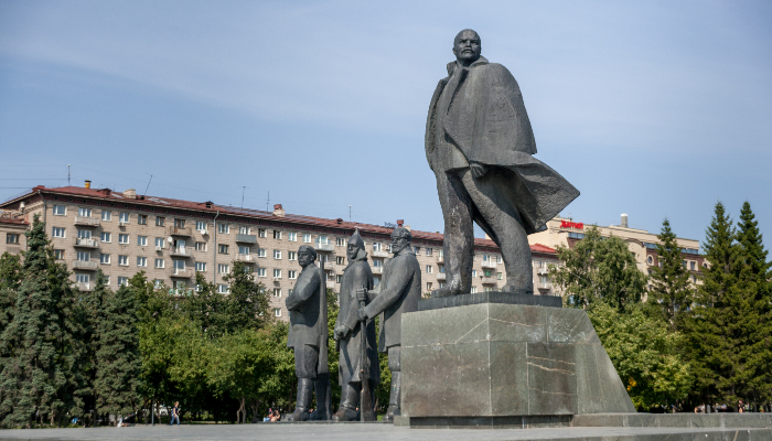 Colour photo of Lenin Square, Novosibirsk, Russia. The monument has a statue of Lenin on a pedestal with a worker, a soldier, and a peasant to the left.