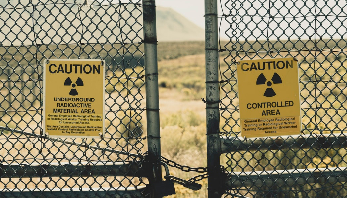 Colour photo of 2 radiation warning signs on a padlocked fence. One sign has the words 'Caution — controlled area' and a radiation warning symbol.
