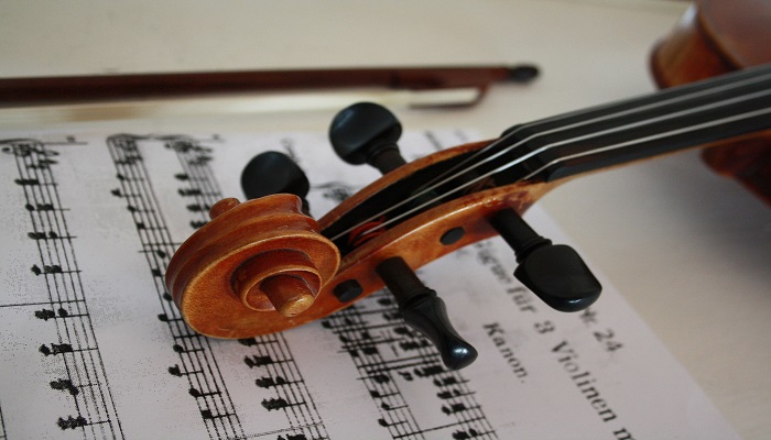 Colour photo of a violin with its scroll (spiral-shaped top) resting on a music sheet.