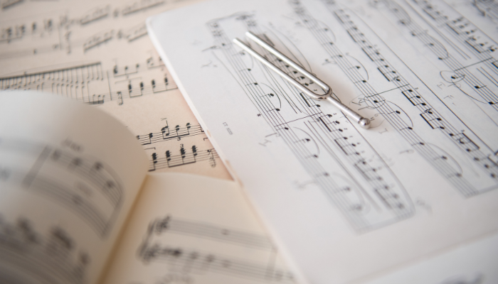 Colour photo of a tuning fork sitting on top of 3 pieces of sheet music.
