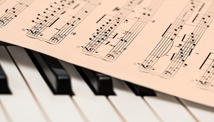 Colour photo of sheet music lying on the keys of a piano keyboard.