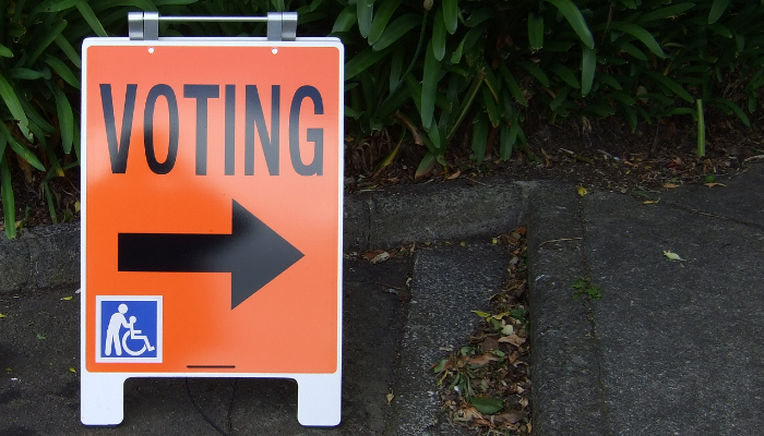 Colour photo of a bright orange sign with the word 'Voting' with an arrow below it pointing to where to vote.