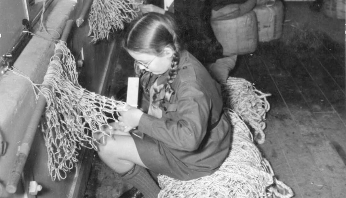 Black and white photo showing a young member of the Girl Guides making camouflage nets.