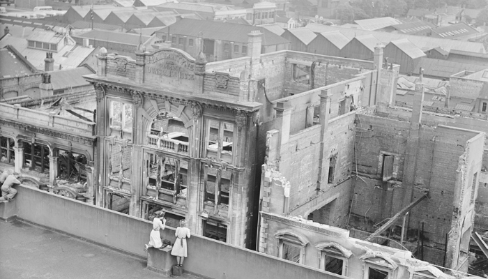 Image: People on roof top overlooking ruins of J. Ballantyne and Company Dunstable House building (https://www.aucklandmuseum.com/discover/collections/record/1052493?k) by Mr Tudor Washington Collins. Collection: Auckland War Memorial Museum. Ref: PH-2013-7-TC-B760-03. Image cropped.
