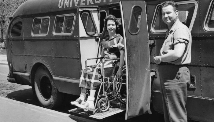 Black and white photo of a student with polio in a wheelchair using a bus lift.