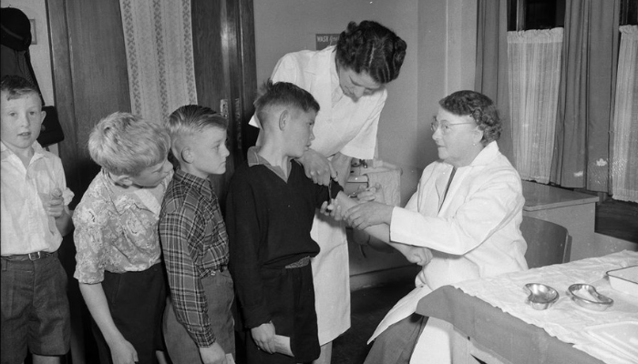 Image: Children being vaccinated against polio, Newtown School, Wellington (https://natlib.govt.nz/records/23186041). Collection: Alexander Turnbull Library. Ref: 1/2-040570-F. Image cropped.

