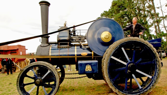 Colour photo of John Fowler's steam-powered ploughing machine. It has 4 wheels and an engine with a funnel in the front. 