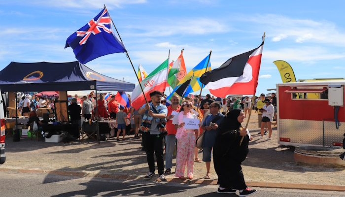 2021 photo of a group of people at Ōhinemutu on Waitangi Day. They hold flags including the Tino Rangatira flag, New Zealand flag, and for other countries.