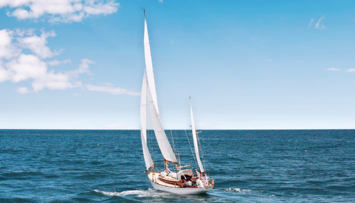 Colour photo of a small boat at sea. It is using its 3 open sails to catch the wind and power it forward.