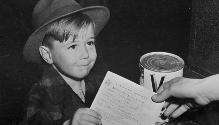 1943 black and white photo of a child being handed a small book with writing on it saying 'War ration book two'.