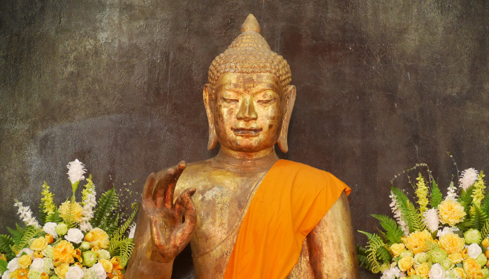 Close up colour photo of golden a Buddha statue from head to waist. One hand is raised. The statue is in the Wat Suthat temple in Bangkok, Thailand.