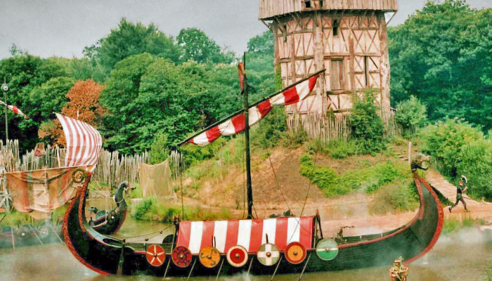 2011 colour photo showing reconstructed Viking longships sitting on a lake, with an old wooden tower in the background.