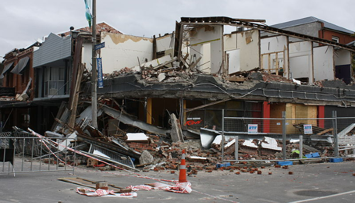 Colour photo of Colombo and Peterborough Streets, Christchurch after it was damaged by an earthquake in 2011. It shows damaged storefronts and bricks fallen on the street.