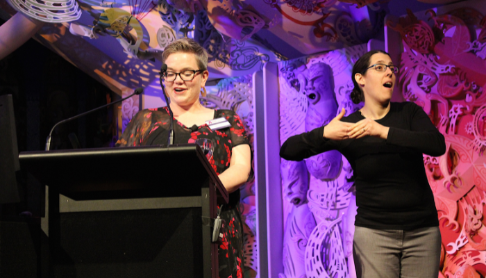 Image: MC Kathryn Tyree and sign language interpreter Bridgette Strid (45531783391) (https://commons.wikimedia.org/wiki/File:MC_Kathryn_Tyree_and_sign_language_interpreter_Bridgette_Strid_(45531783391).jpg) by Catalyst Open Source on Wikimedia Commons. CC BY-SA 2.0 (https://creativecommons.org/licenses/by-sa/2.0/deed.en). Image cropped.
