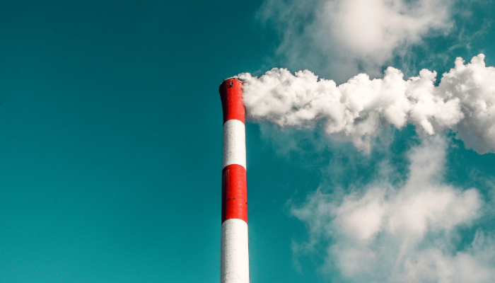 Colour photo of a tall red and white factory chimney emitting thick smoke into a clear blue sky.