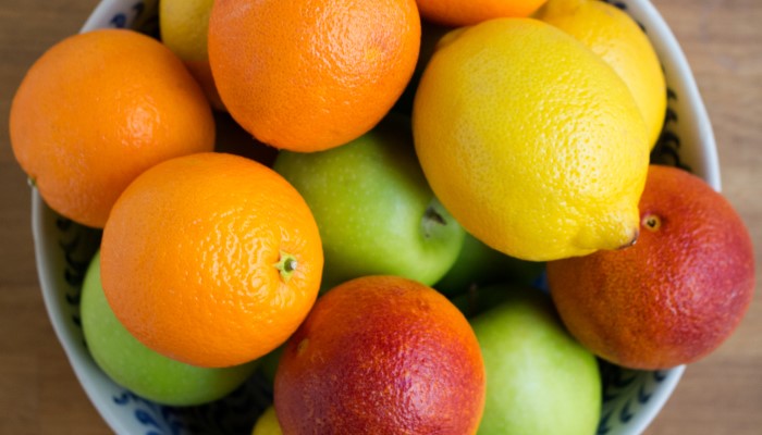 Close up colour photo of a bowl of fruit. The fruit includes oranges, lemons, and green apples.