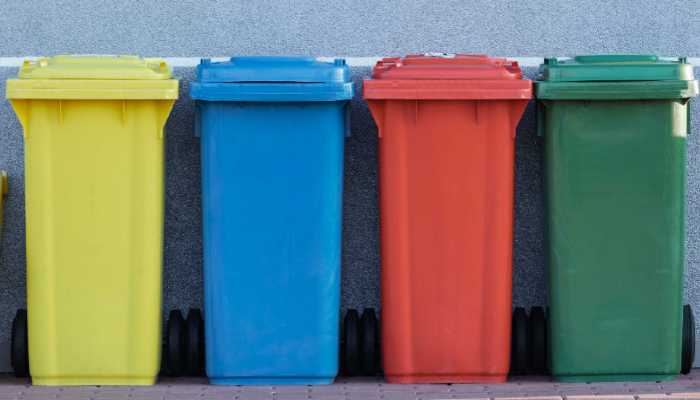 Colour photo of 4 recycling bins — one of each in yellow, blue, red and green colour for different materials to be recycled.