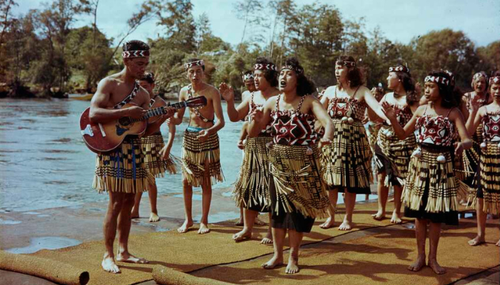 Colour photo showing a kapa haka group performing next to a body of water.