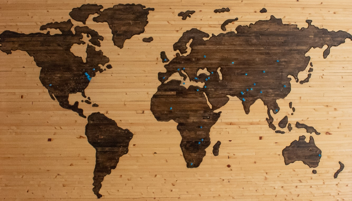 Photo of a wooden map of the world with blue pins marking important cities.