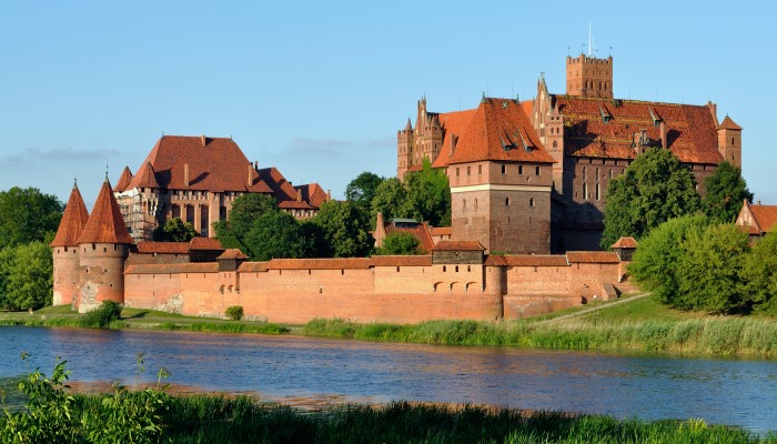 Colour photo of Malbork Castle in Poland from across the Nogat river. It shows the castle complex surrounded by a wall.