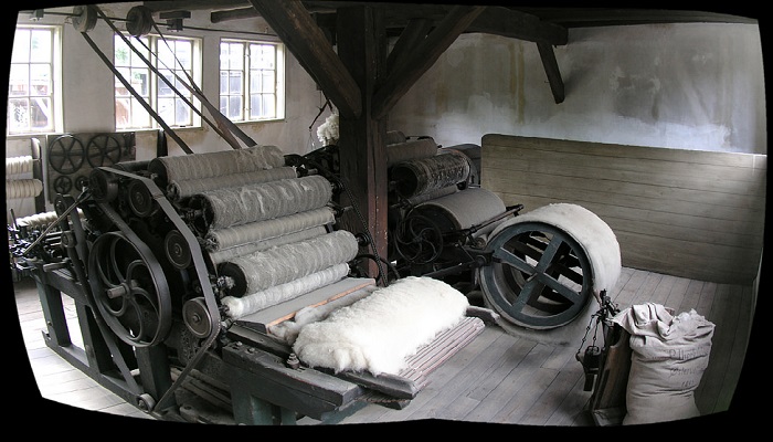 Photo of an early wool carding machine with an engine and lots of rollers. There is also a batch of wool to be processed.