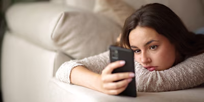 young woman lying on sofa looking at phone