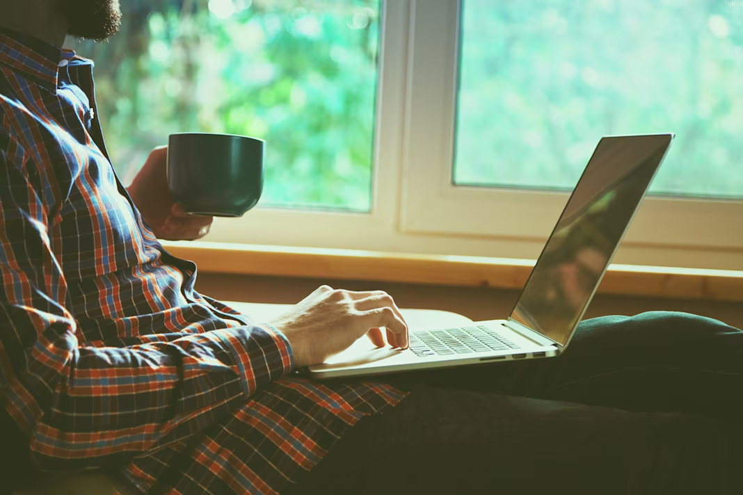 man at home with a laptop and a mug of tea or coffee