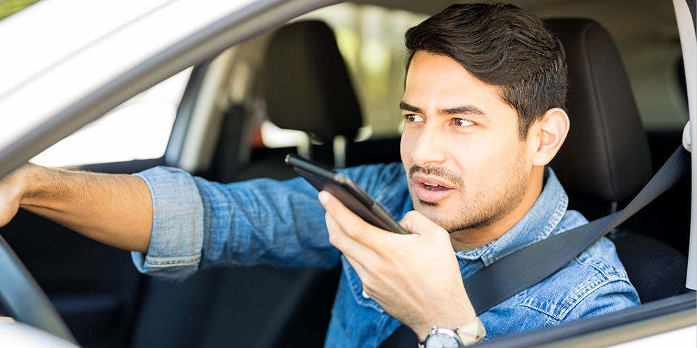 man having conversation on loudspeaker with phone while driving car