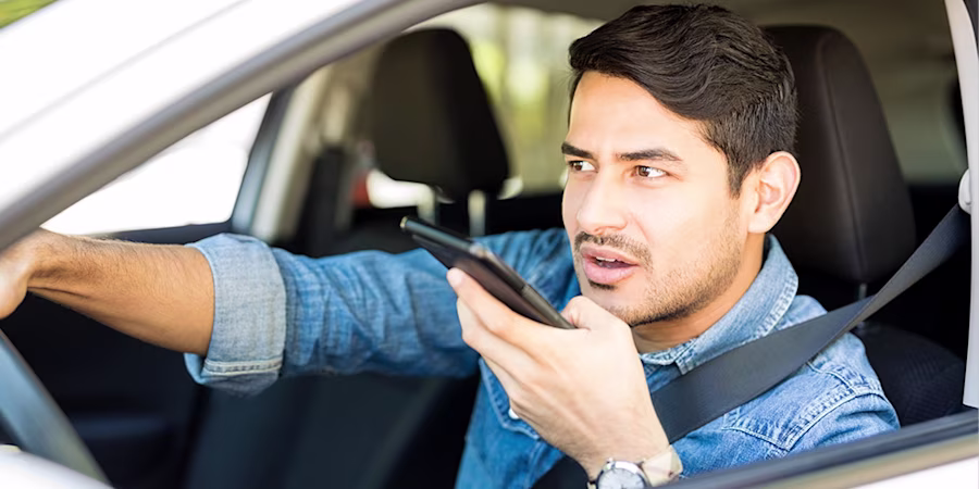 man having conversation on loudspeaker with phone while driving car
