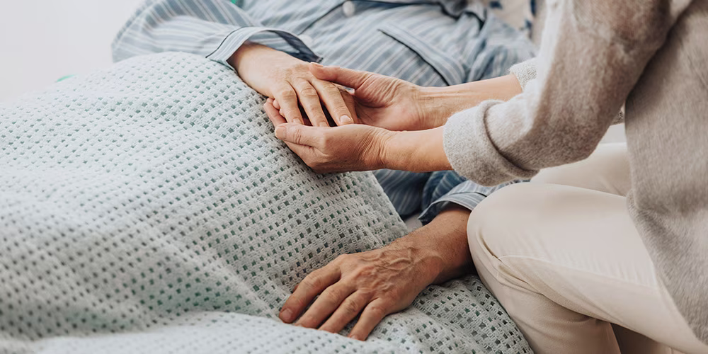 woman holding hand of man in hospital bed