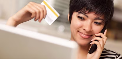 Woman talking on the phone holding a credit card and smiling