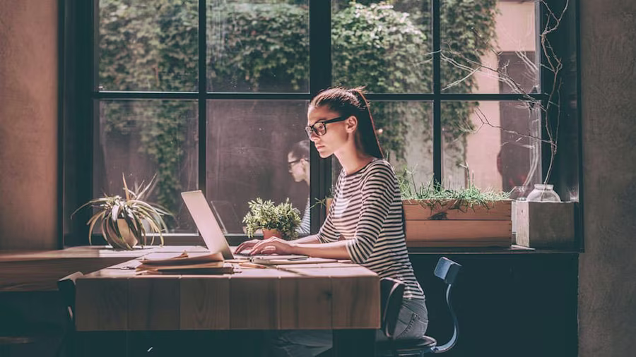 A woman on a laptop on a desk next to a window