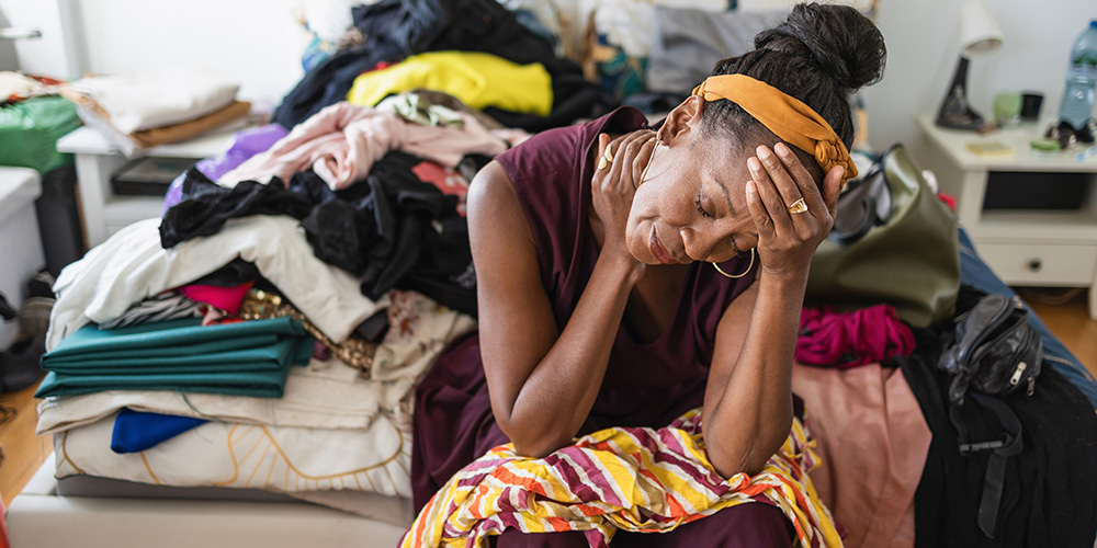 A distressed woman surrounded by piles of clothes and clutter