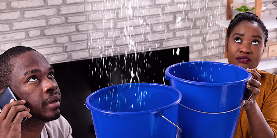Couple holding buckets under leaking ceiling