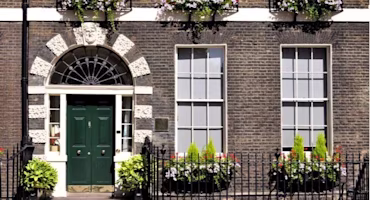The front of a brickhouse with a cast iron fence and flowery planters