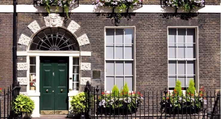 The front of a brickhouse with a cast iron fence and flowery planters