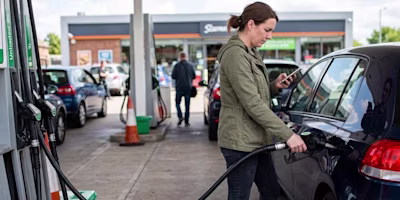 woman looking at her phone while fuelling her vehicle