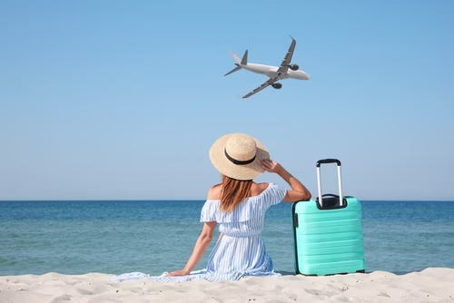 Woman on beach watch a plane with suitcase