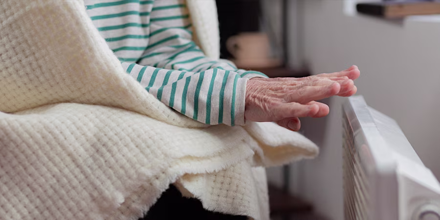 Older woman warming her hands near a radiator